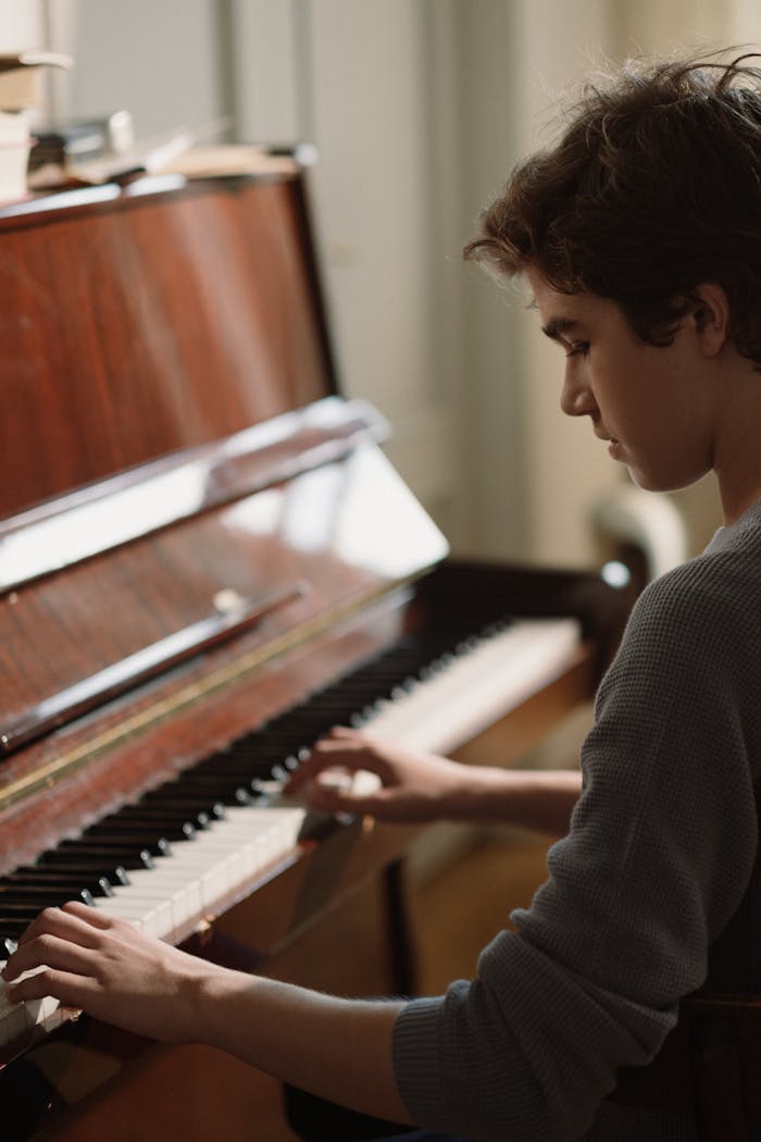 Close-up of a teenager playing an upright wooden piano indoors.