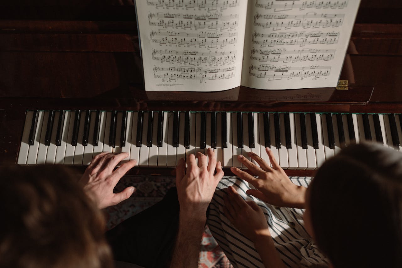 A man and woman playing piano, with music sheets, viewed from above.