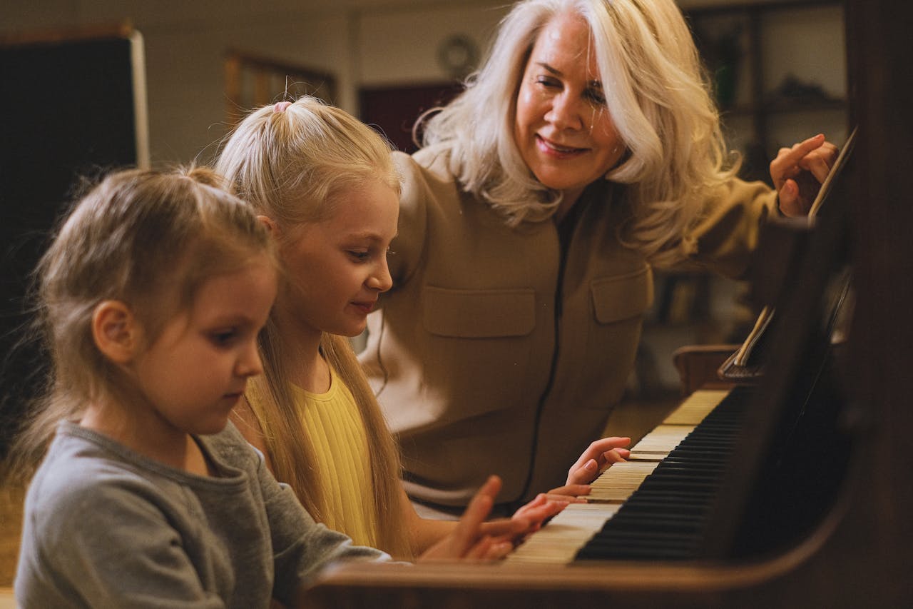 services-02 A grandmother joyfully teaches her granddaughters to play piano indoors, fostering musical growth.