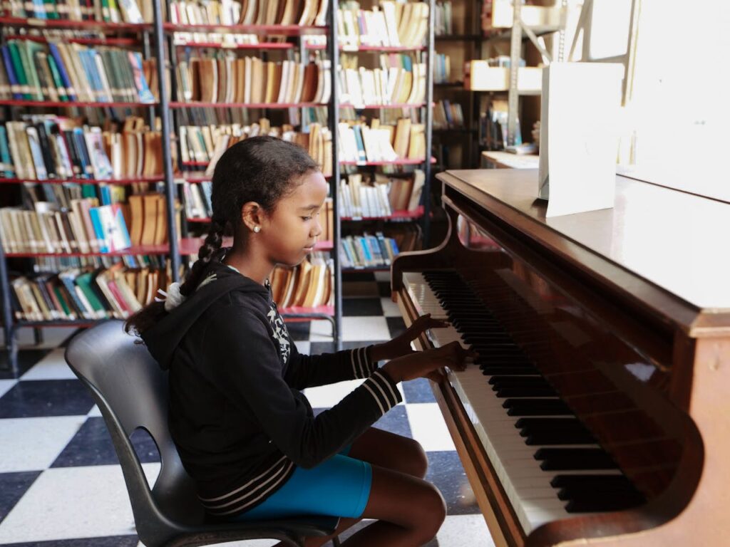 Home A young girl sits at a piano in a library, playing music in a bright and inviting space.