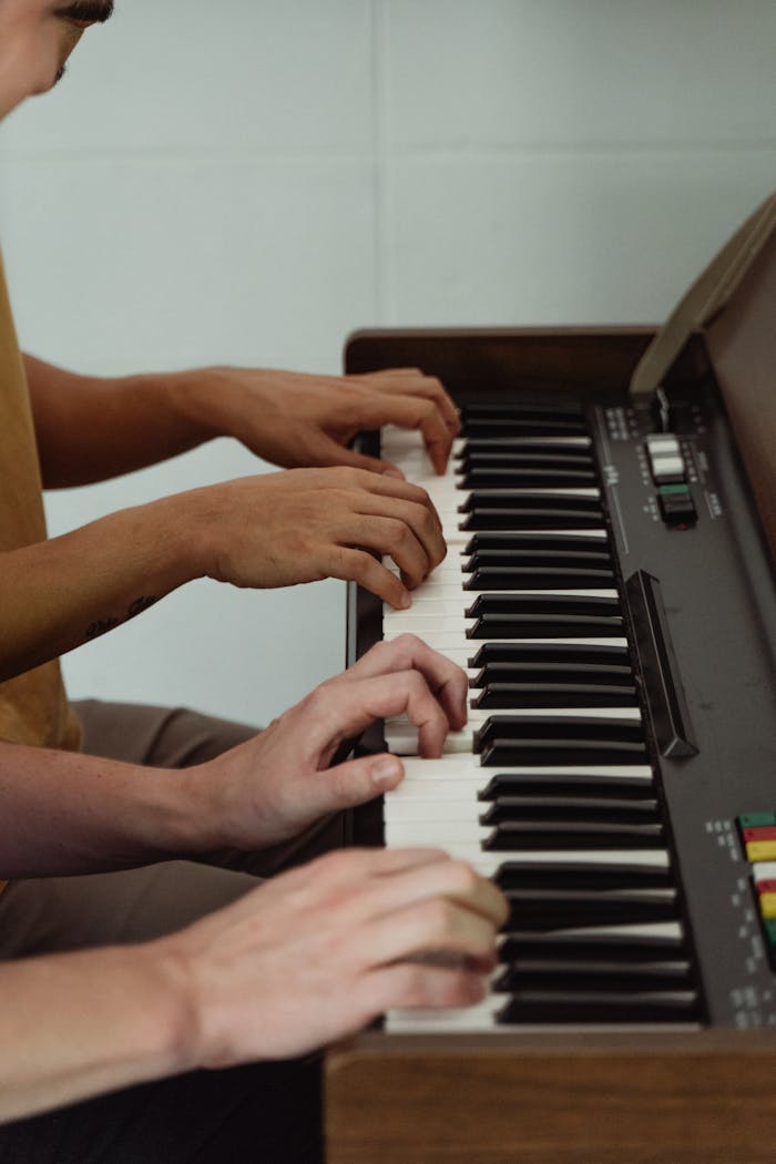 gallery-5 Close-up of two people playing piano, focusing on hands and fingers on keys.