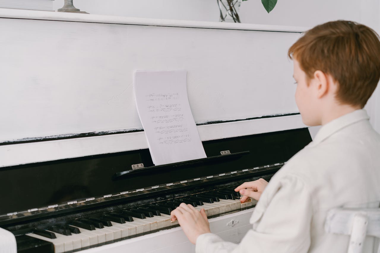 gallery-3 A young boy sits at an upright piano playing music indoors, focused on sheet music.