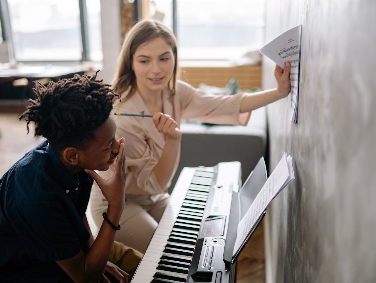 A piano teacher instructs a young student at the keyboard, focusing on music sheets.